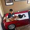 Mochi joined the competition — help win amazing prizes! boy, child, dog, bed, car_bed, red_bed, indoor, room, wall_art, carpet, blue_chair, smiling, shorts, tshirt, pet, fur, happy, playing, sitting, home