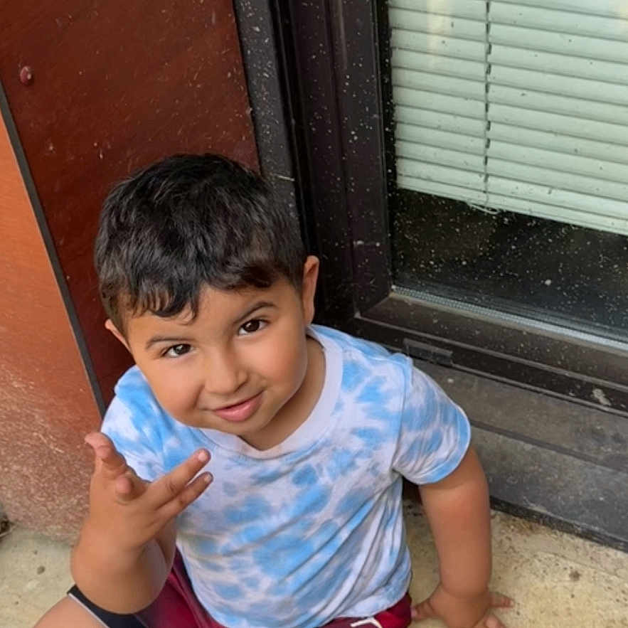 Abdel participe au concours pour gagner de l'argent avec cette photo : blinds, boy, casual_clothing, child, concrete, concrete_step, door, face, ground, hair, hand_gesture, outdoor, person, playful, shirt, shorts, smiling, sneakers, window, young