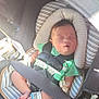 baby, sleeping, car_seat, seatbelt, harness, infant, newborn, hospital_bracelet, green_clothing, striped_cushion, footwear, pacifier, safety, child, transportation, car_interior, sunlight, peaceful, cute, resting