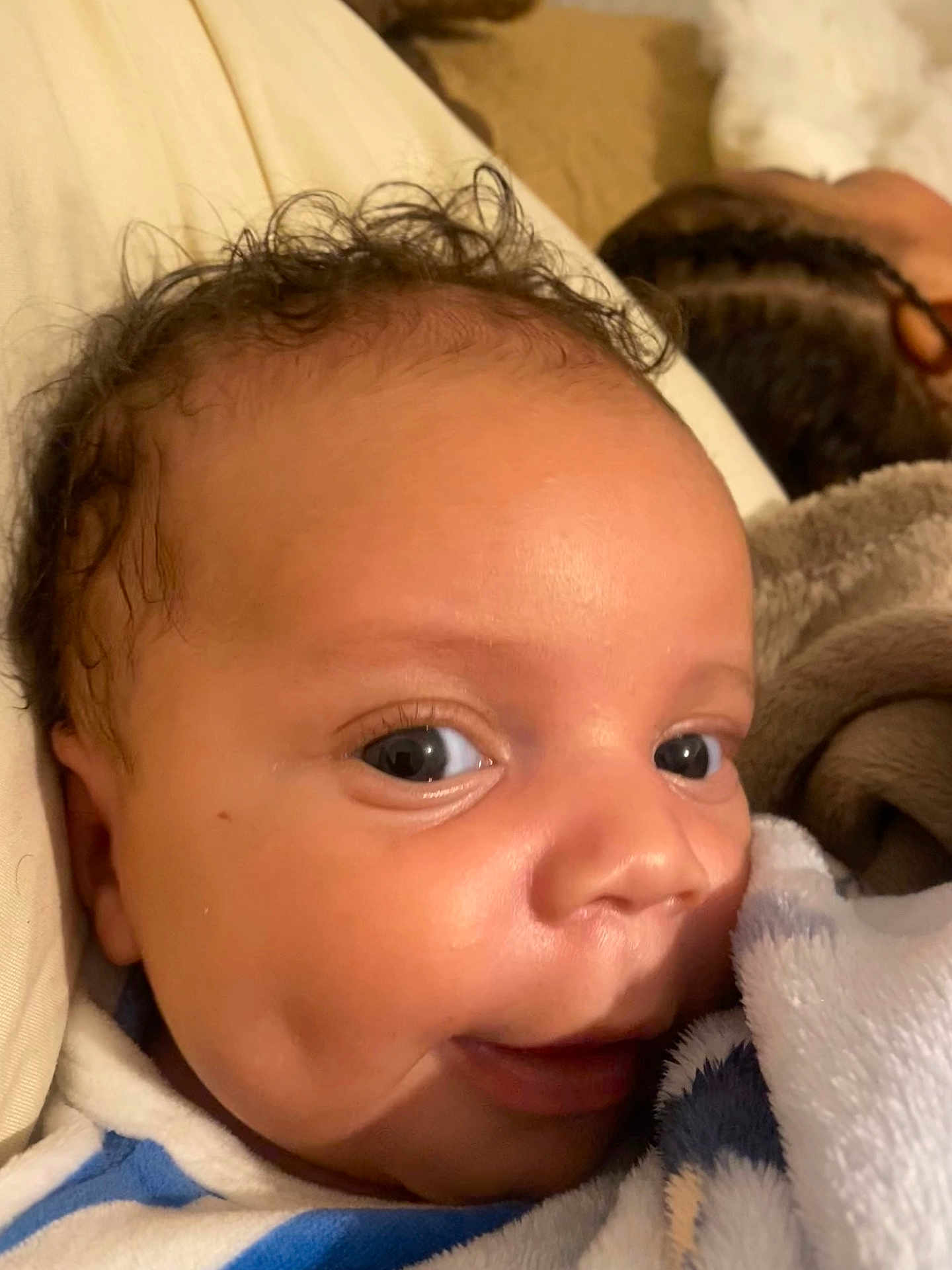 Djaeli participe au concours pour gagner de l'argent avec cette photo : baby, infant, newborn, face, eyes, dimples, smile, curly_hair, blanket, swaddle, close_up, portrait, cheek, skin, cuddly, bed, pillow, parent_in_background, braids, cozy