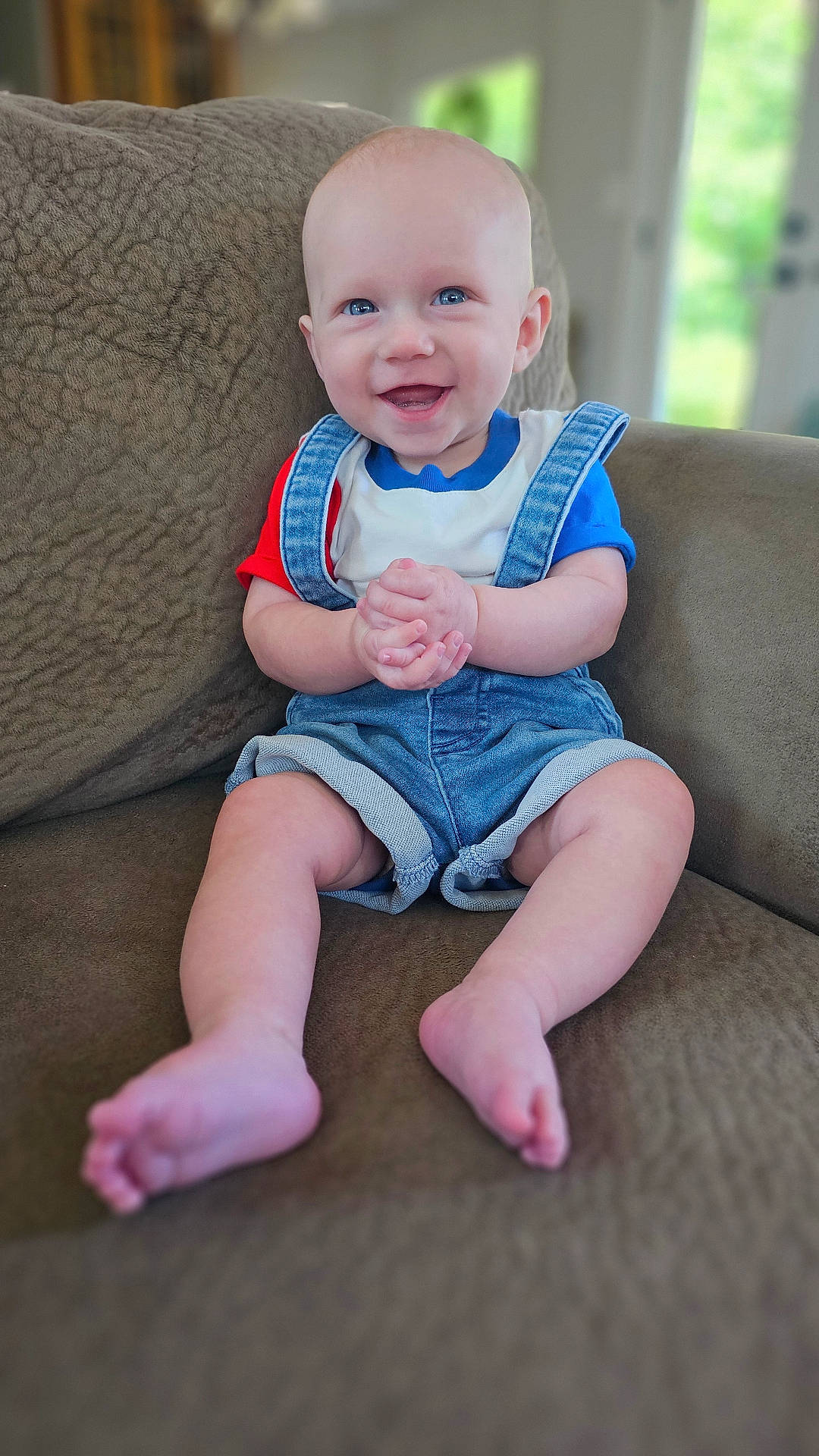 Nash is registered to the contest to win money with this photo: baby, barefoot, blue_eyes, child, clothing, couch, cute, denim_overalls, face, hands, happy, home, indoor, infant, legs, portrait, seated, skin, smile, tshirt