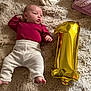 baby, infant, blanket, balloon, number_one, maroon_clothing, cream_pants, lying_down, soft_texture, celebration, cute, cozy, child, newborn, floor, indoors, portrait, resting, one_year, happy