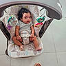 Hanah is registered to the contest to win money with this photo: baby, infant, child, bouncer, baby_seat, buckled, sitting, wide_eyed, curly_hair, gray_shirt, toys, toy_bar, indoor, tiled_floor, playroom, portrait, full_body, chair, sandal, photography