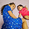 children, siblings, baby, toddler, girl, infant, sister, bed, bedroom, lying_down, smiling, portrait, floral_dress, blue_dress, pink_outfit, curly_hair, long_hair, family, indoor, happy