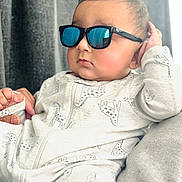 Siraj is registered to the contest to win money with this photo: baby, casual, child, closeup, cozy, cute, face, fashion, giraffe_pattern, hand, indoor, infant, onesie, person, portrait, reflection, relaxing, soft_lighting, sunglasses, young_child