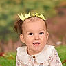 baby, child, portrait, smiling, happy, face, eyes, mouth, hair_bows, yellow_bows, ponytail, floral_dress, collar, clothing, sitting, front_facing, outdoor_background, blurred_background, studio_portrait, infant