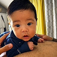 Ozias joined the competition — help win amazing prizes! adult_hands, baby, blue_shirt, child, closeup, clothing, curtains, cute, expression, eyes, face, hair, hands, holding, indoor, infant, person, portrait, skin, yellow_curtains