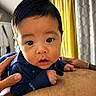adult_hands, baby, blue_shirt, child, closeup, clothing, curtains, cute, expression, eyes, face, hair, hands, holding, indoor, infant, person, portrait, skin, yellow_curtains