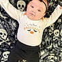 baby, infant, halloween, onesie, black_bow, headband, skull_pattern, blanket, cute, lying_down, black_pants, pumpkin, bats, holiday, celebration, child, costume, smiling, portrait, indoors