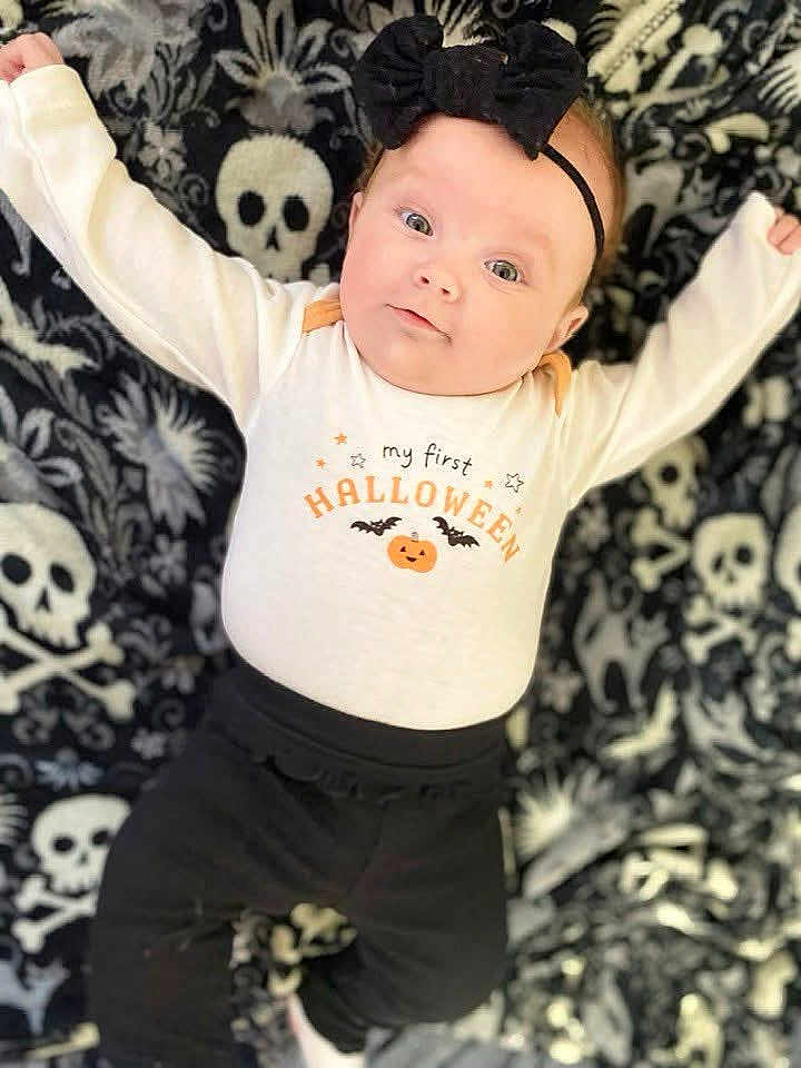 Allison joined the competition — help win amazing prizes! baby, infant, halloween, onesie, black_bow, headband, skull_pattern, blanket, cute, lying_down, black_pants, pumpkin, bats, holiday, celebration, child, costume, smiling, portrait, indoors
