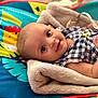 baby, infant, blanket, play_mat, colorful, smiling, face, child, cute, clothing, portrait, soft_texture, indoors, happy, young, person, resting, cozy, bright, eyes