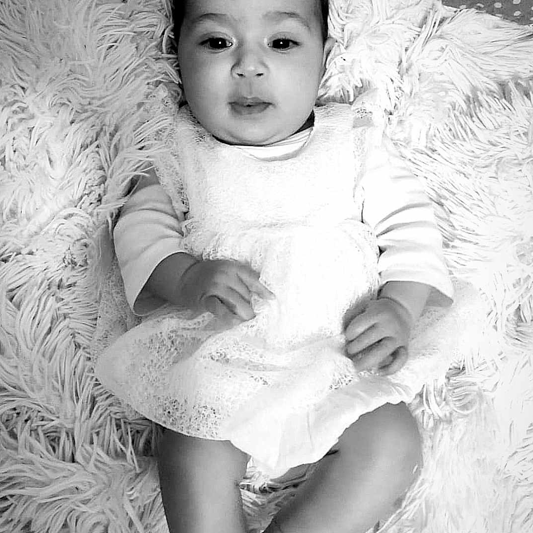 Arinasse participe au concours pour gagner de l'argent avec cette photo : baby, barefoot, black_and_white, carpet, child, cute, dress, face, feet, fluffy_rug, hands, indoor, infant, lace, looking, monochrome, portrait, sitting, white_dress, young_child