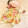 baby, infant, child, dress, headband, bow, fruit_pattern, colorful, white_background, soft_surface, lying_down, motion_blur, hand, footwear, socks, cute, indoors, clothing, fabric, portrait