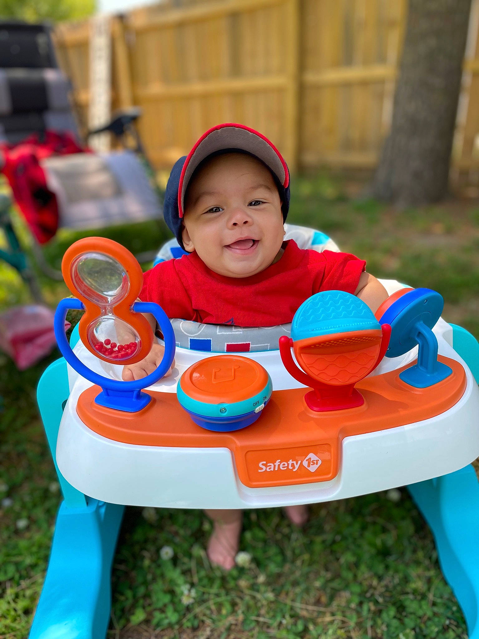 Kaison is registered to the contest to win money with this photo: baby, baby_toddler_clothing, chair, child, event, face, fun, grass, happy, headwear, joy, leisure, outdoor_furniture, person, play, recreation, sharing, shorts, sitting, smile