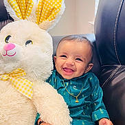 Shaurya is registered to the contest to win money with this photo: baby, bunny, chair, child, cuddly, cute, face, golden_necklace, hand, happy, indoor, infant, leather, plush_toy, portrait, smiling, stuffed_animal, teal_clothing, toy, yellow