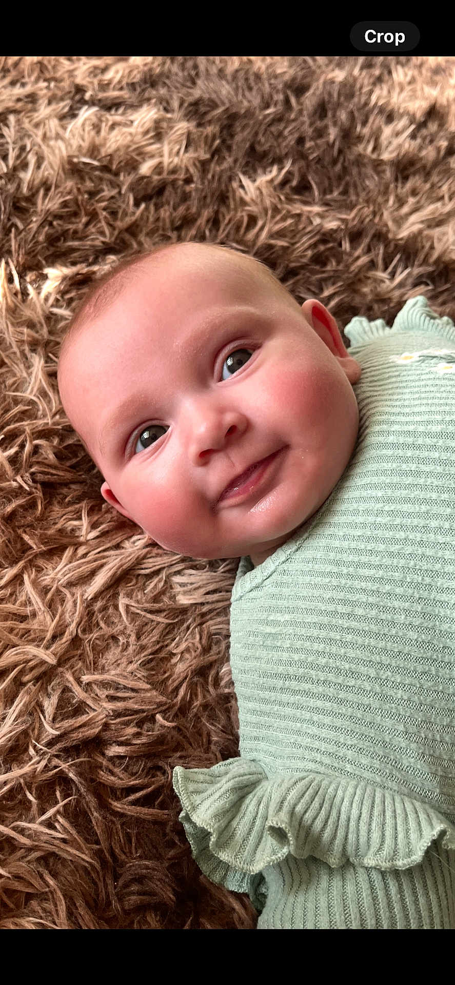 Florence is registered to the contest to win money with this photo: baby, infant, smiling, face, eyes, cheeks, mint_green, ribbed_clothing, ruffles, lying_down, fluffy_rug, brown_rug, close_up, portrait, cute, happy, child, soft_texture, indoor, adorable
