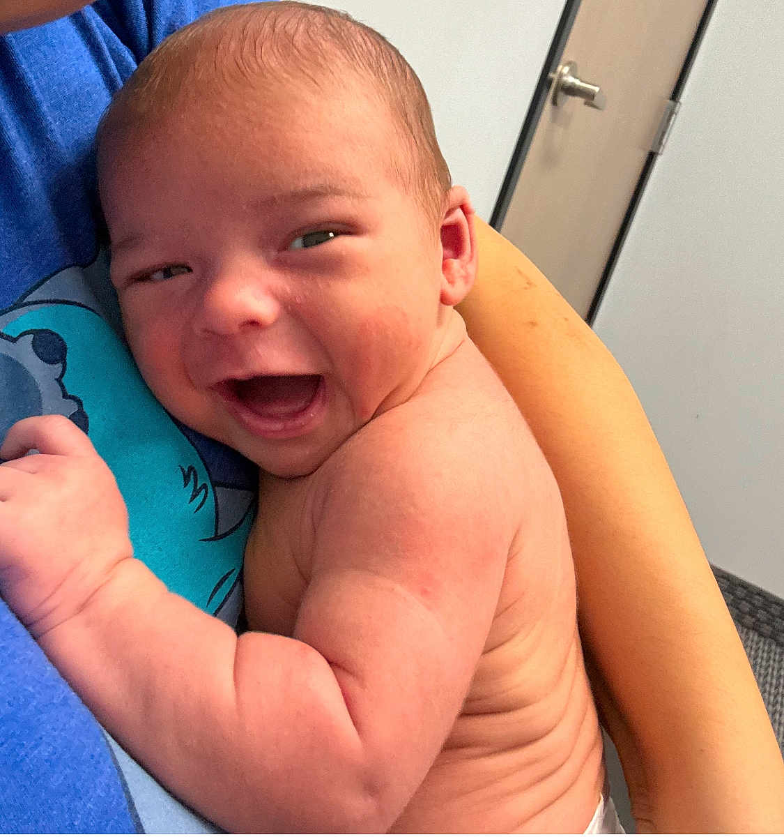 Wayne joined the competition — help win amazing prizes! baby, smiling, infant, child, person, skin, arm, hand, face, expression, happy, holding, blue_shirt, indoor, door, wrinkles, newborn, closeup, parent, comfort