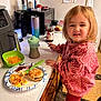 toddler, child, kitchen, breakfast, plate, eggs, bacon, biscuit, sippy_cup, sweatshirt, pink_crocs, countertop, jar, strawberry_preserves, knife, chair, note, refrigerator, food, person