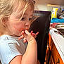 toddler, child, finger_licking, messy, orange_sauce, kitchen, cabinet, countertop, chair, white_shirt, blonde_hair, curly_hair, indoor, candid, portrait, person, skin, hand, face, young_child