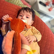 Anastasia participe au concours pour gagner de l'argent avec cette photo : baby, child, pacifier, stuffed_animal, toy, cushion, quilted, orange, pink, yellow, striped_clothing, lying_down, indoor, soft_toy, infant, cute, closeup, face, hand, relaxed