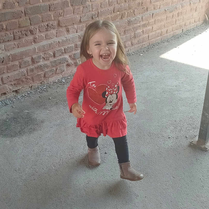 Celia a rejoint le concours — aidez-le/la à gagner de superbes lots ! boots, brick_wall, casual_clothing, child, concrete_floor, cute, daylight, full_body, happy, laughing, long_hair, minnie_mouse, outdoor, person, playful, red_dress, smiling, toddler, walking, young_girl