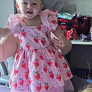 Daenerys joined the competition — help win amazing prizes! toddler, child, pink_dress, strawberry_pattern, curly_hair, smiling, earrings, indoor, person, hand, adult, bed, shelf, bag, toys, furniture, clothing, happy, portrait, cute