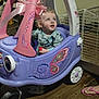 toddler, child, toy_car, pink_bow, curly_hair, indoor, wooden_floor, purple, pink, playtime, cute, looking_up, face, footwear, flip_flops, pet_gate, home, person, wheel, clothing