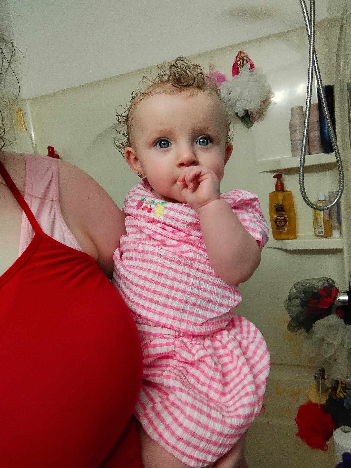 Daenerys is registered to the contest to win money with this photo: baby, child, person, blue_eyes, curly_hair, pink_dress, bathroom, shower, adult, holding, thumb_sucking, earrings, facial_expression, curious, clothing, skin, indoor, portrait, cute, human