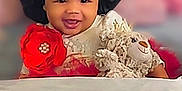 Heavenly is registered to the contest to win money with this photo: baby, child, smiling, black_bonnet, red_flower, plush_toy, teddy_bear, pillow, red_roses, soft_toys, indoors, cute, happy, portrait, infant, clothing, face, headwear, decor, cozy