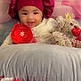 baby, child, smiling, bonnet, flower, red_flower, pillow, teddy_bear, heart, crown, plush_toy, indoor, cute, portrait, infant, soft_toy, decor, happy, headwear, lying_down