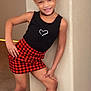 Isreãl is registered to the contest to win money with this photo: child, girl, smiling, posing, black_tank_top, red_checkered_skirt, gray_socks, indoor, carpet, wall, hair_up, choker_necklace, young, confident, casual_clothing, person, portrait, playful, happy, fashion