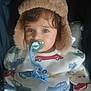 toddler, child, pacifier, hat, fur_hat, clothing, sitting, indoor, cute, face, blue_eyes, patterned_clothes, car_pattern, baby, comfort, infant, warm_clothing, portrait, young_child, cozy