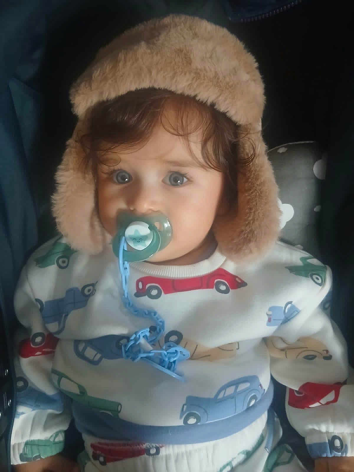 Adam a rejoint le concours — aidez-le/la à gagner de superbes lots ! toddler, child, pacifier, hat, fur_hat, clothing, sitting, indoor, cute, face, blue_eyes, patterned_clothes, car_pattern, baby, comfort, infant, warm_clothing, portrait, young_child, cozy