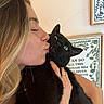 person, cat, black_cat, green_eyes, kiss, facial_expression, hand, ring, indoor, wall_art, frame, blonde_hair, close_up, pet, affection, unimpressed_cat, home, portrait, light_skin, decor