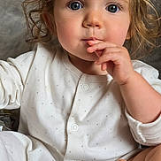Florence is registered to the contest to win money with this photo: child, toddler, baby, face, hair, curly_hair, onesie, foot, hand, fingers, indoor, couch, blanket, clothing, cute, portrait, sitting, expression, skin, infant