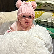 Maïzy participe au concours pour gagner de l'argent avec cette photo : baby, pink_hat, pom_poms, blanket, pillow, floral_pattern, infant, cute, cozy, indoor, child, soft_texture, knitwear, smiling, face, portrait, toddler, warm_clothing, home, resting