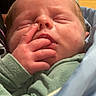 newborn, baby, infant, sleeping, face, portrait, hand, fingers, green_clothing, blanket, swaddled, held, close_up, indoors, person, skin, eyes_closed, nose, mouth, cozy