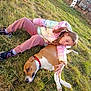 child, dog, grass, outdoor, playground, slide, jacket, sneakers, pet, relaxing, sunny, casual_clothing, friendship, lying_down, nature, fence, daytime, animal, young_girl, leisure