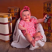 Bresil a rejoint le concours — aidez-le/la à gagner de superbes lots ! baby, child, smiling, pink_headband, gingham_clothing, blanket, chair, wooden_floor, vintage_suitcases, brown_background, happy, sitting, portrait, indoor, cute, small_object, person, footwearless, head, infant