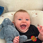 Noah is registered to the contest to win money with this photo: baby, bodypart, clothing, couch, cushion, face, finger, furniture, hand, happy, head, homedecor, laughing, mouth, person, photography, plush, portrait, t_shirt, toy