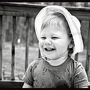 Cameron joined the competition — help win amazing prizes! toddler, child, smiling, hat, short_sleeve_shirt, tools_pattern, outdoor, deck, wooden_rail, black_and_white, portrait, happy, cute, young_child, person, daytime, hair, face, clothing, baby