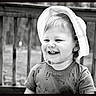 toddler, child, smiling, hat, short_sleeve_shirt, tools_pattern, outdoor, deck, wooden_rail, black_and_white, portrait, happy, cute, young_child, person, daytime, hair, face, clothing, baby