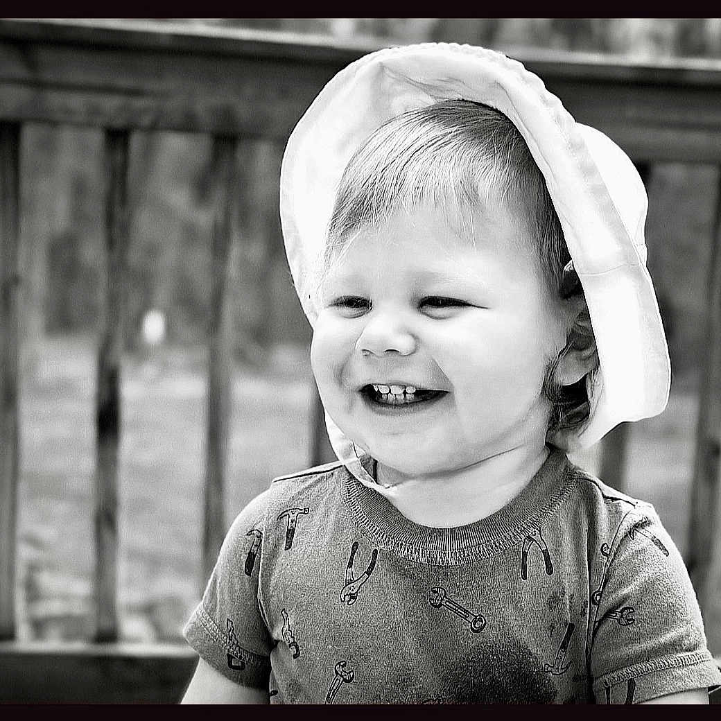 Cameron joined the competition — help win amazing prizes! toddler, child, smiling, hat, short_sleeve_shirt, tools_pattern, outdoor, deck, wooden_rail, black_and_white, portrait, happy, cute, young_child, person, daytime, hair, face, clothing, baby