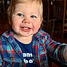 baby_teeth, background_blur, blue_eyes, candid, casual, child, closeup, clothing, cute, happy, indoor, messy_face, person, plaid_shirt, portrait, seated, smile, toddler, warm_lighting, young_child