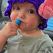 Renesmae joined the competition — help win amazing prizes! toddler, child, hat, knitted_hat, purple, pink_flower, lollipop, blue_lollipop, green_dress, rosy_cheeks, cute, portrait, face, hand, indoor, car_interior, curious, young_child, person, closeup