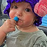 toddler, child, hat, knitted_hat, purple, pink_flower, lollipop, blue_lollipop, green_dress, rosy_cheeks, cute, portrait, face, hand, indoor, car_interior, curious, young_child, person, closeup