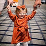 child, toddler, orange_dress, bow, holding_hands, walking, outdoor, sunlight, shadows, boardwalk, happy, person, legs, feet, adult_hands, casual_clothing, daytime, smile, cute, playful
