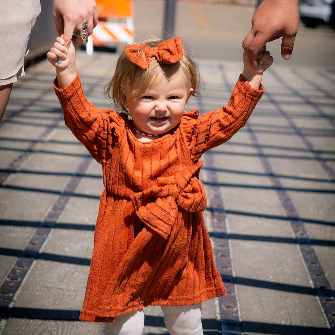 Renesmae joined the competition — help win amazing prizes! child, toddler, orange_dress, bow, holding_hands, walking, outdoor, sunlight, shadows, boardwalk, happy, person, legs, feet, adult_hands, casual_clothing, daytime, smile, cute, playful