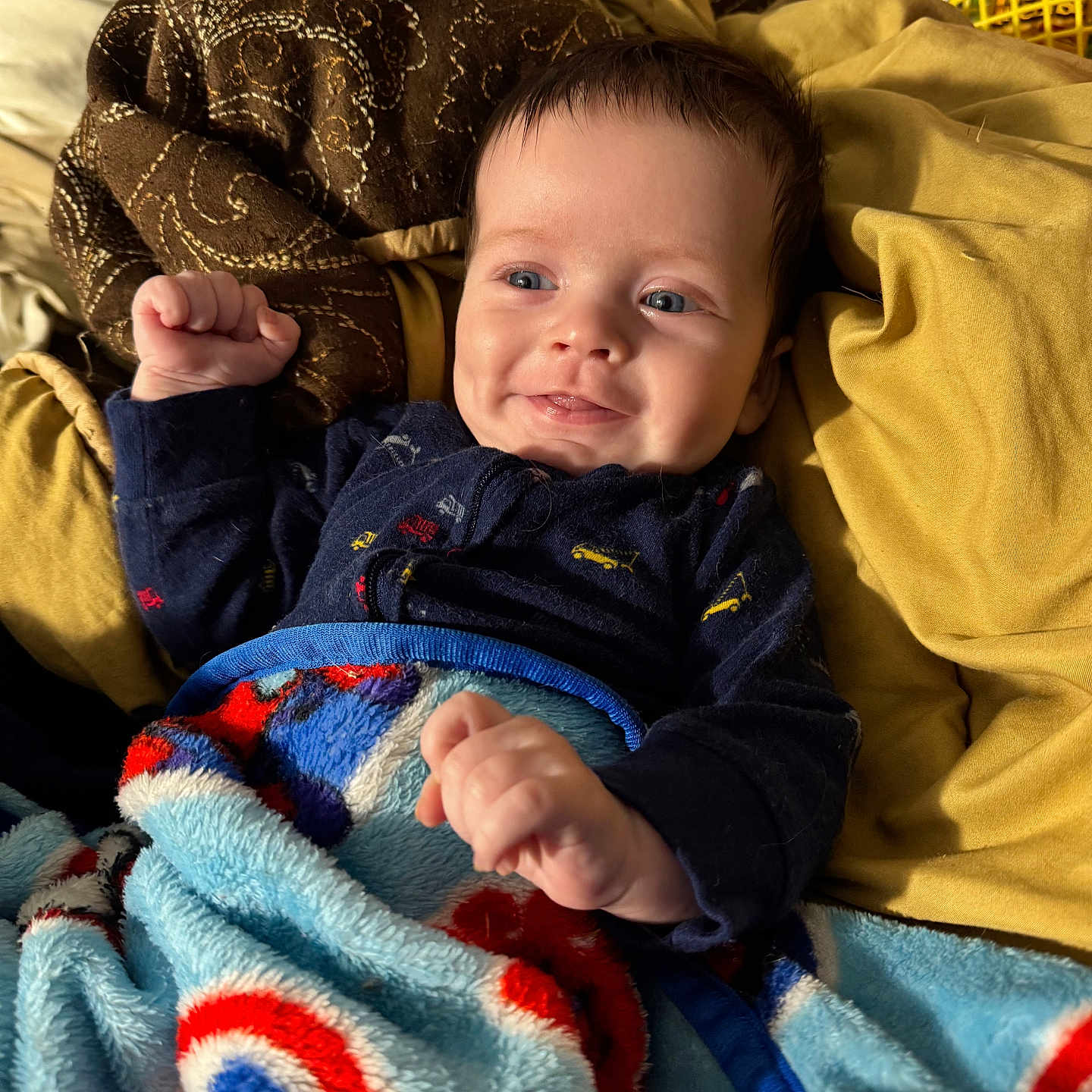 Denver is registered to the contest to win money with this photo: baby, blanket, blue, brown, child, clothing, comfortable, cozy, cute, face, hands, happy, indoor, infant, pillow, portrait, red, resting, smiling, yellow