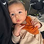 Hady joined the competition — help win amazing prizes! baby, infant, child, person, face, eyes, hand, clothing, bib, sitting, indoor, black_clothing, beige_clothing, orange_bib, nike_logo, closeup, cute, soft_light, chair, background